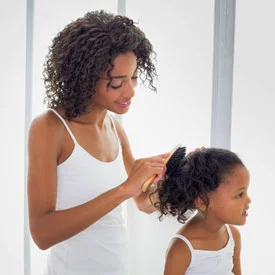 african american mom brushing daughters hair before head lice treatment